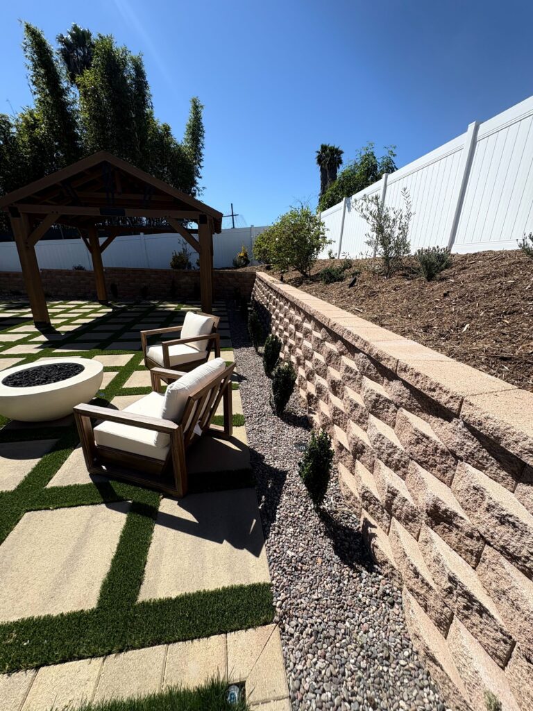 Paver-and-turf grid patio with round fire feature, pergola, and gravel drainage strip at the retaining wall toe in Vista, CA. Install It Direct project.