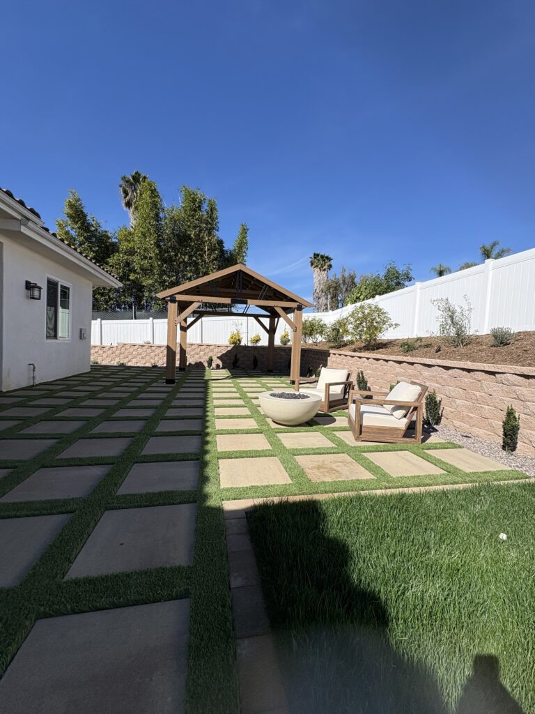 Finished paver patio with timber pergola, fire-bowl seating, and segmental retaining wall with drought-tolerant plantings in Vista, CA. Install It Direct project.