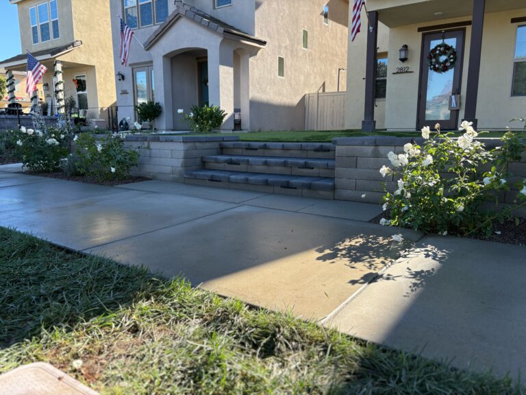 Front yard of a residential property showing a segmental concrete block retaining wall with integrated steps up to raised turf and entry porches. Escondido project by Install It Direct.