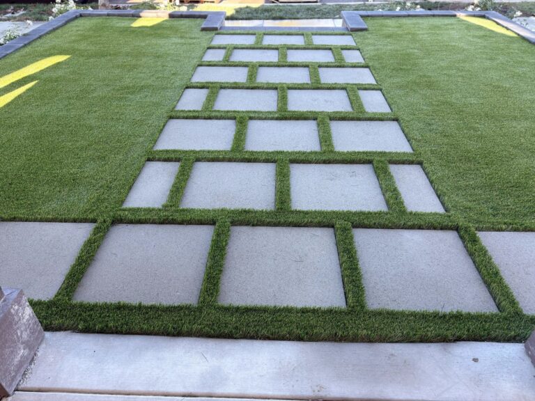 Finished backyard installation showing square concrete pavers set in a geometric grid with artificial turf strips between units. Escondido project by Install It Direct.