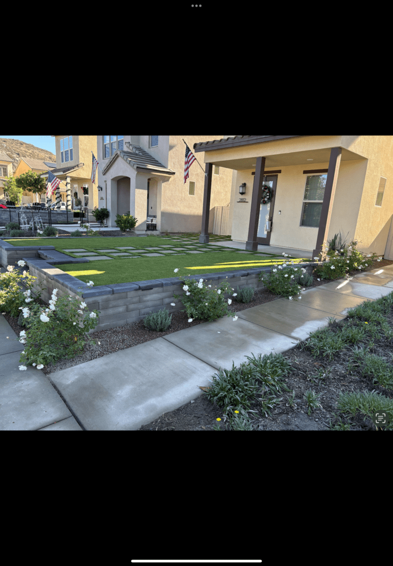 Raised front-yard artificial turf installation bordered by a low segmental retaining wall with square paver stepping stones set into the turf. Escondido project by Install It Direct.