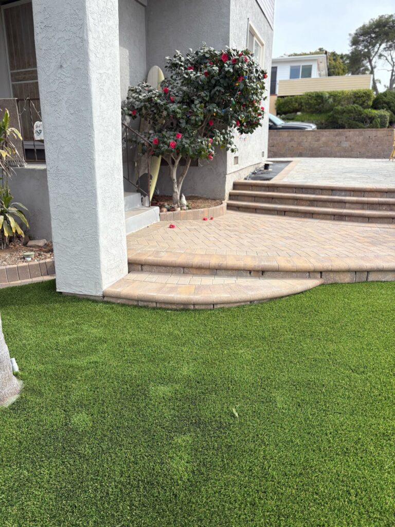 Finished artificial-turf lawn below curved paver steps at the raised Ocean Beach entry.