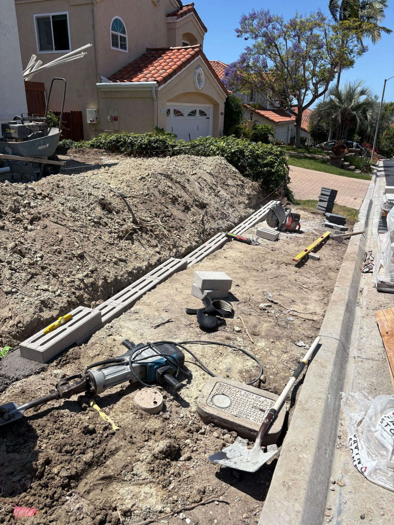 Front-yard excavation and base preparation along a driveway edge for a segmental retaining wall. Soil stockpile and...
