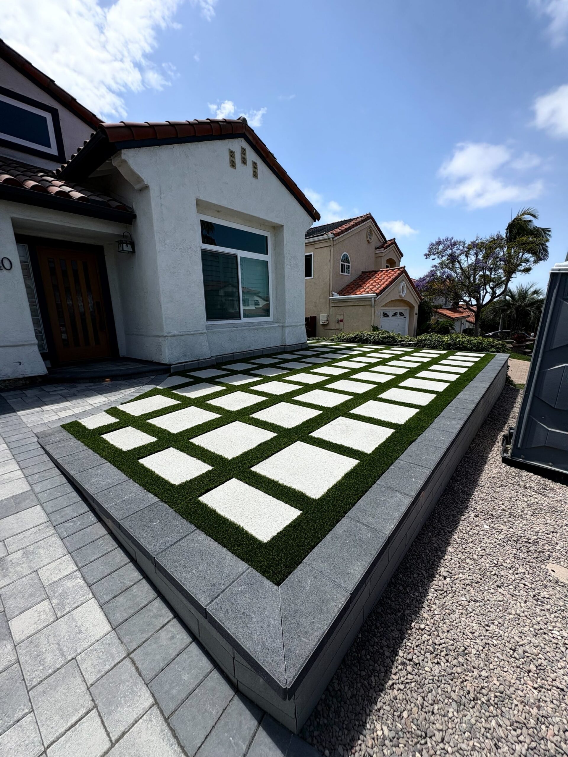 Completed front-yard installation featuring large square concrete pavers set in a checkerboard pattern with artificial...