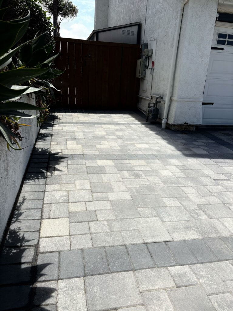 Newly installed interlocking paver driveway and adjoining walkway in a gray mixed-tone ashlar pattern with a darker...