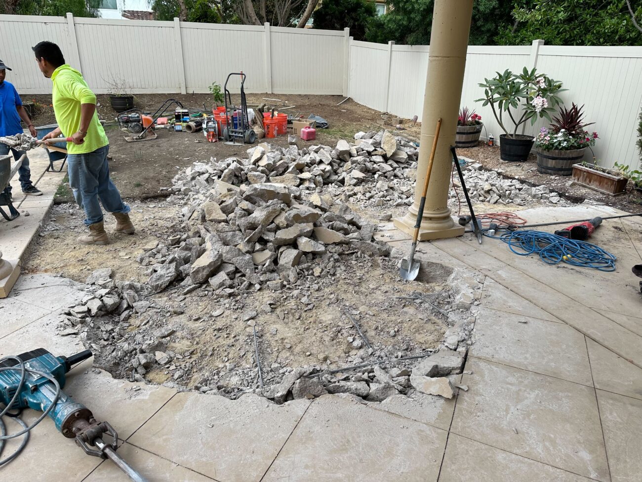 Active demolition of an existing concrete/paved patio is underway with a central area removed and a large pile of broken...