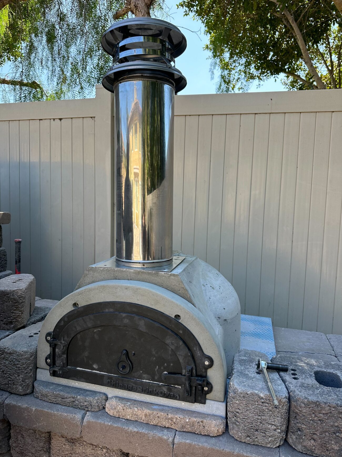 Masonry wood-fired pizza oven with a stainless steel chimney installed on a base of segmental concrete blocks and...
