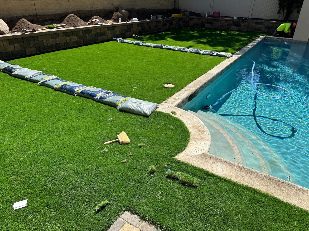 Backyard pool area showing artificial turf being installed adjacent to concrete pool coping; turf seams are held down...