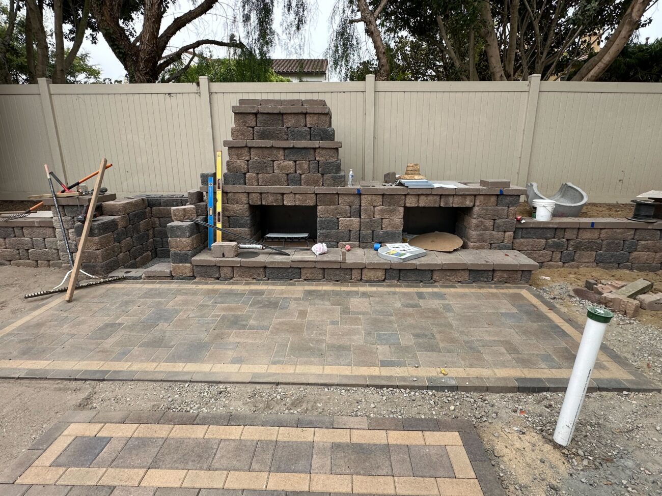 Paver patio with newly installed interlocking pavers in front of a segmental block outdoor kitchen/fireplace under...