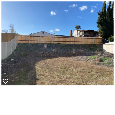 Residential backyard showing a sloped yard with exposed dirt and sparse natural grass up to a new wooden fence. Existing...