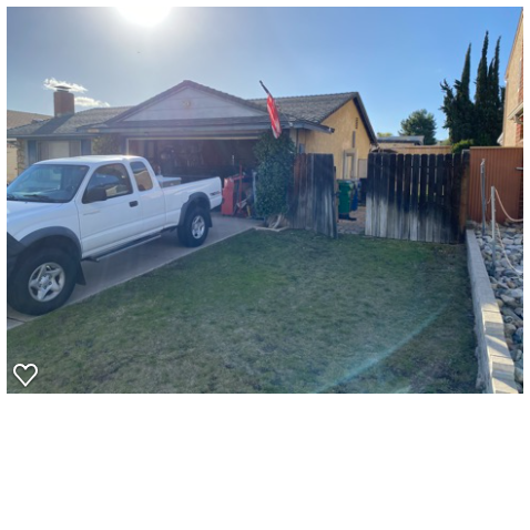 Front yard of a single-family home showing a patchy natural grass lawn adjacent to a concrete driveway with a work truck...