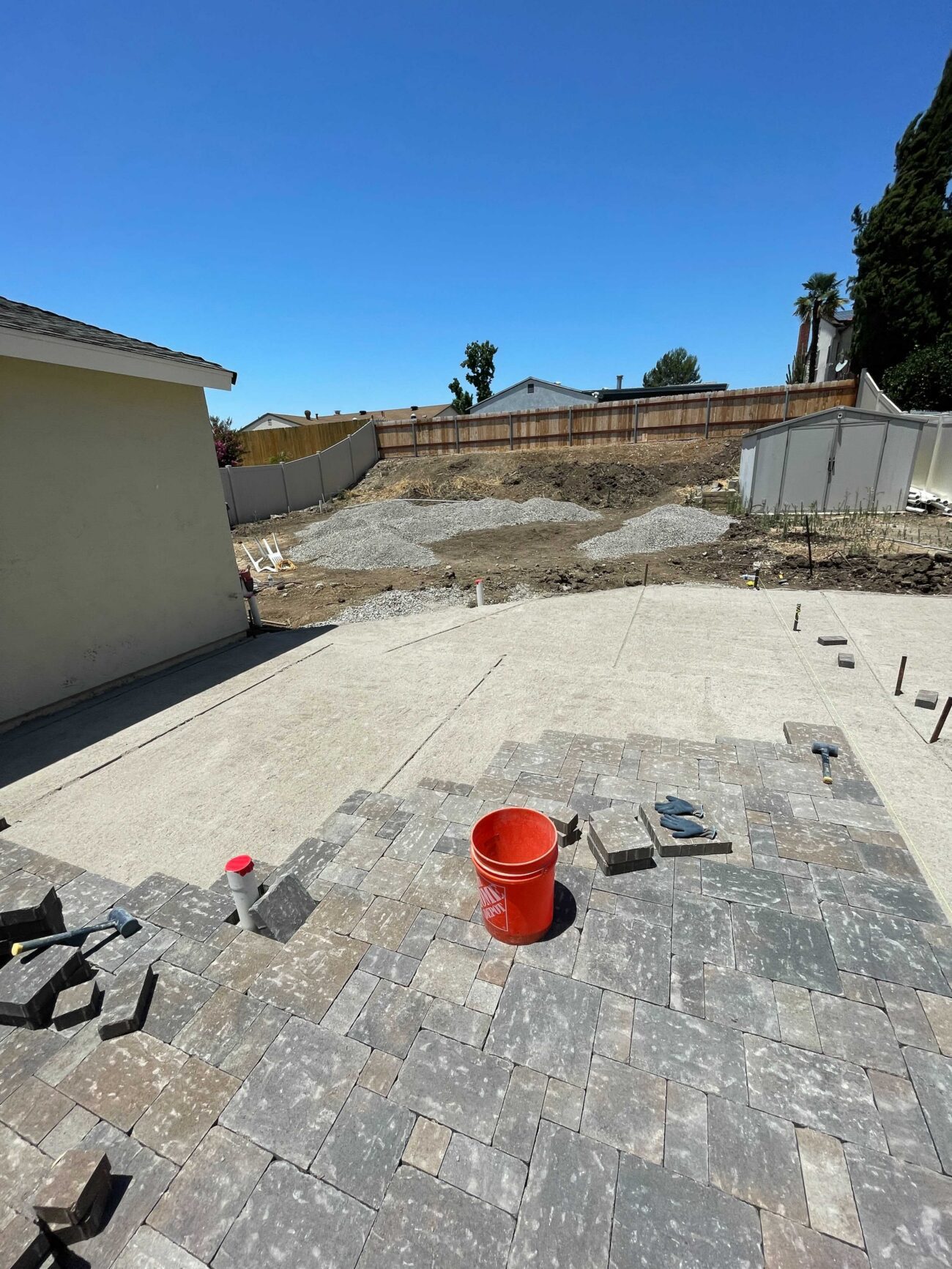 Backyard paver patio installation in progress: interlocking concrete pavers are being laid adjacent to an existing...