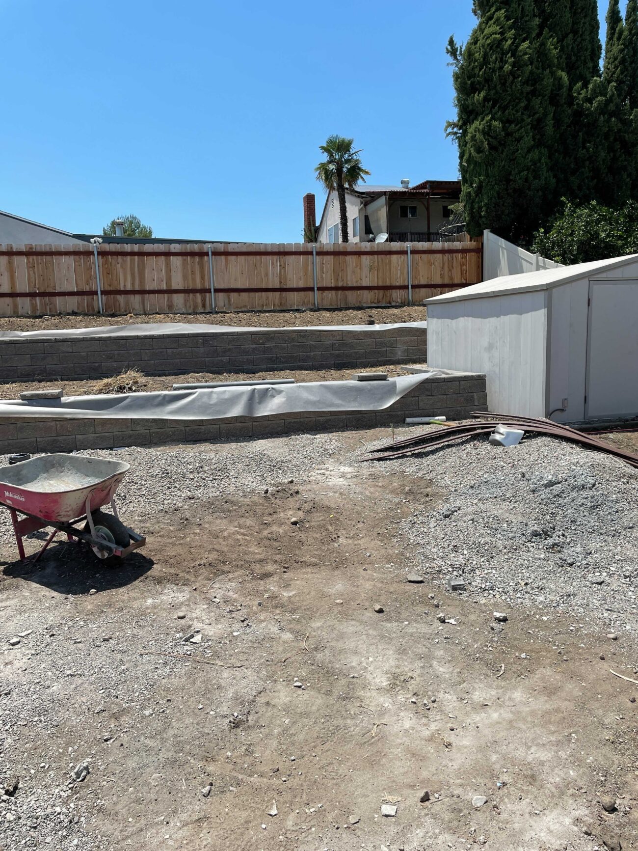 Backyard construction scene showing newly built segmental retaining walls with compacted gravel and dirt base....