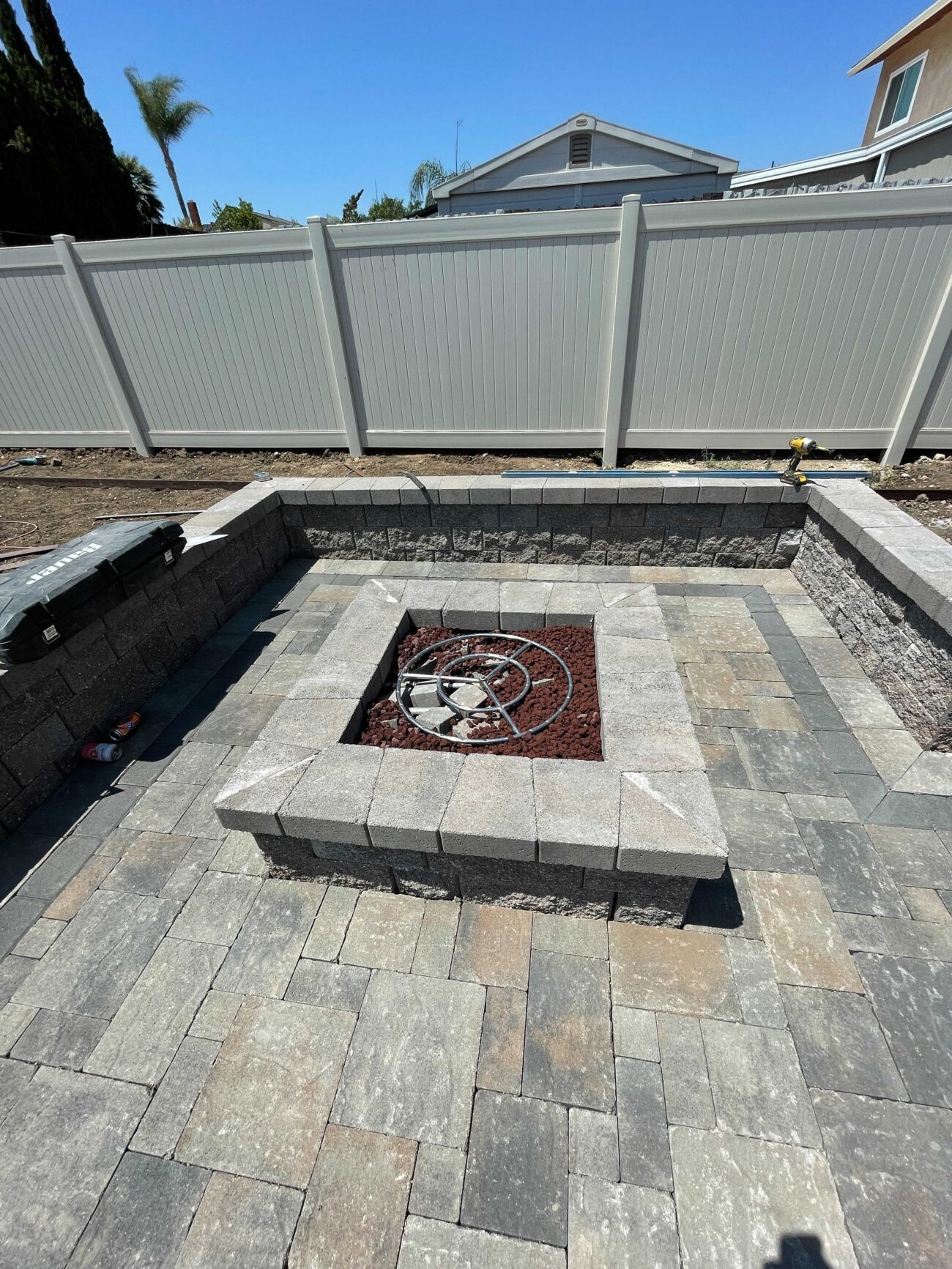 Backyard paver patio with a recessed square fire pit and a low segmental retaining/seating wall. Interlocking concrete...