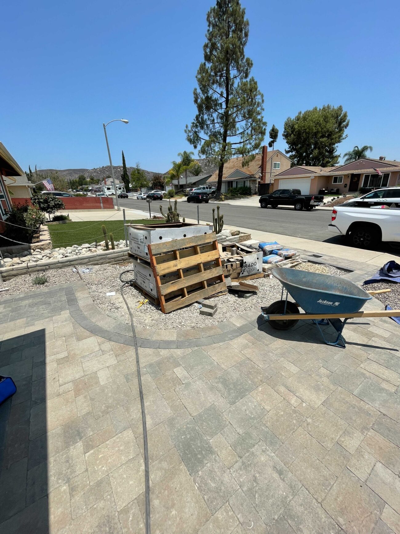 Front yard paver patio installation in progress showing interlocking pavers mostly laid with a curved border defining a...