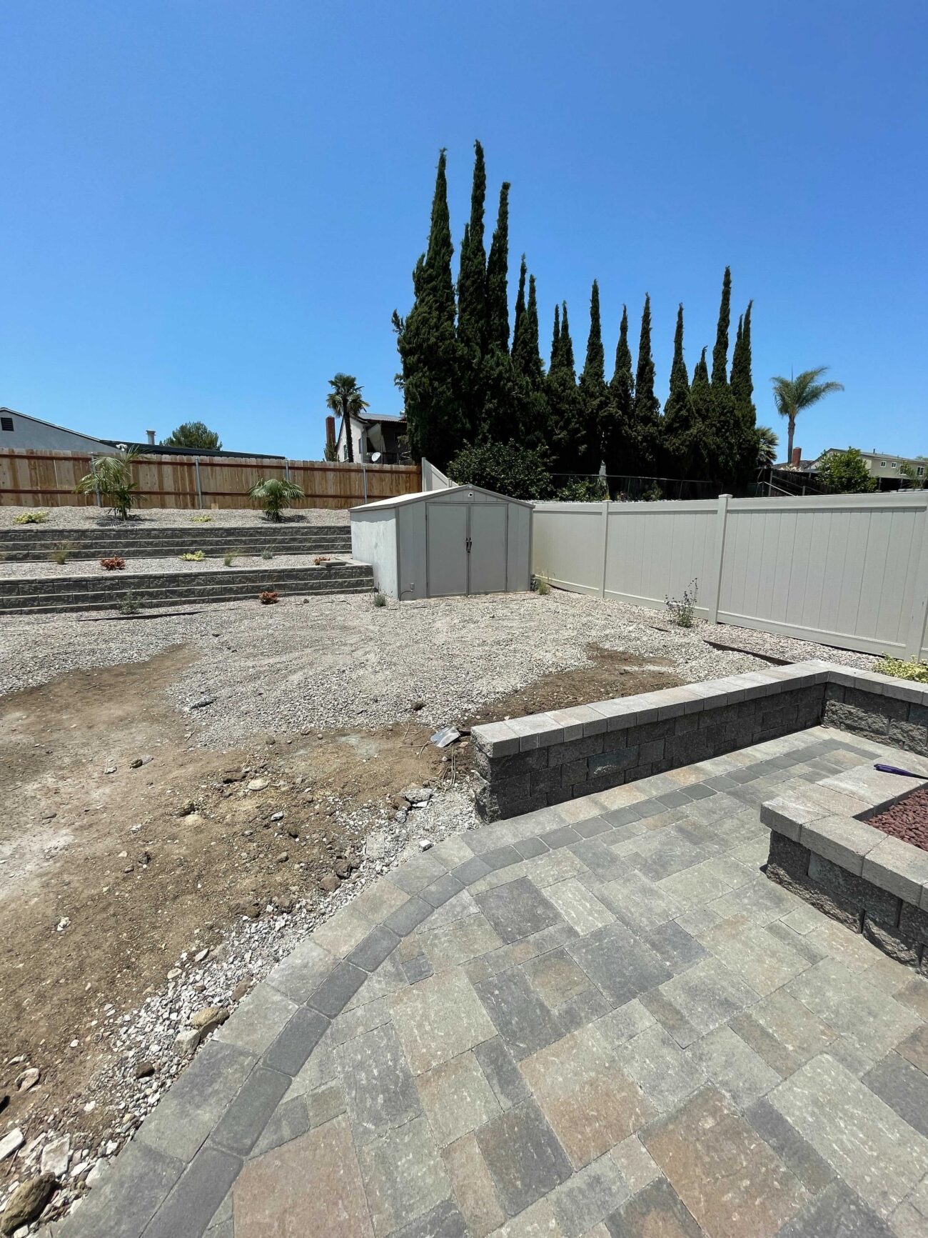 Residential backyard showing a newly installed interlocking paver patio with a low segmental retaining/seat wall in the...