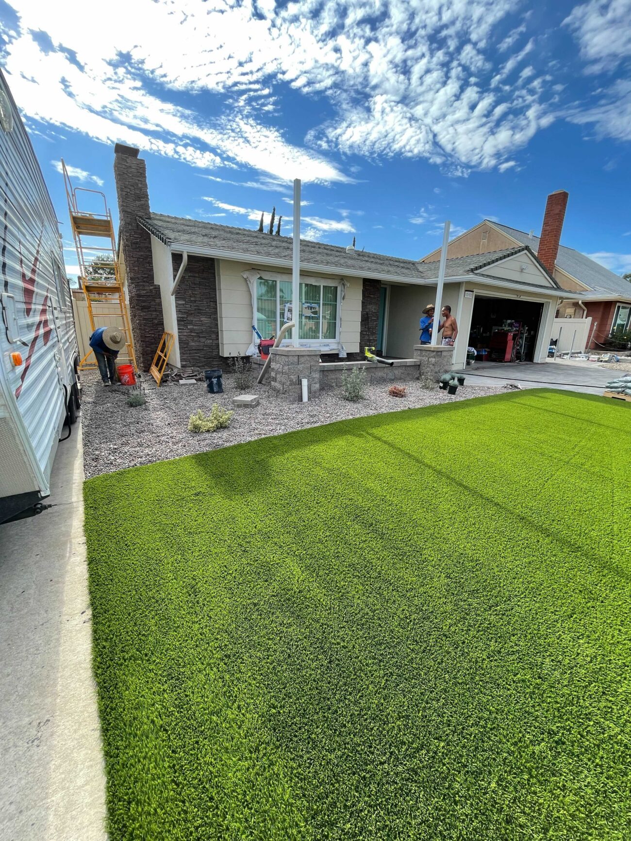 Front-yard artificial turf installation in progress: newly laid synthetic turf covers the lawn area with gravel mulch...