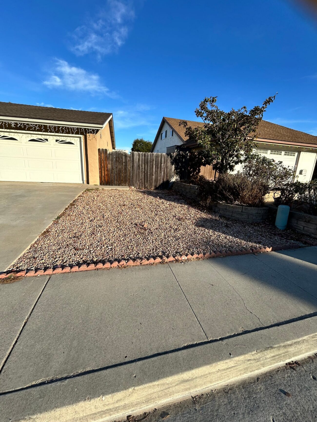 The original front yard: aging tan gravel with scalloped edging, beside the existing block retaining-wall planters and...