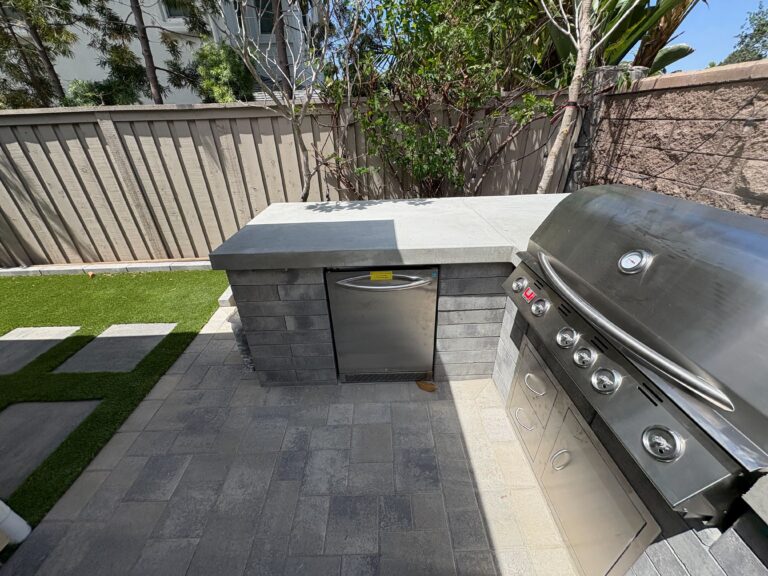 Outdoor kitchen detail showing the concrete counter, stainless appliances, paver patio, turf, and stepping stones.