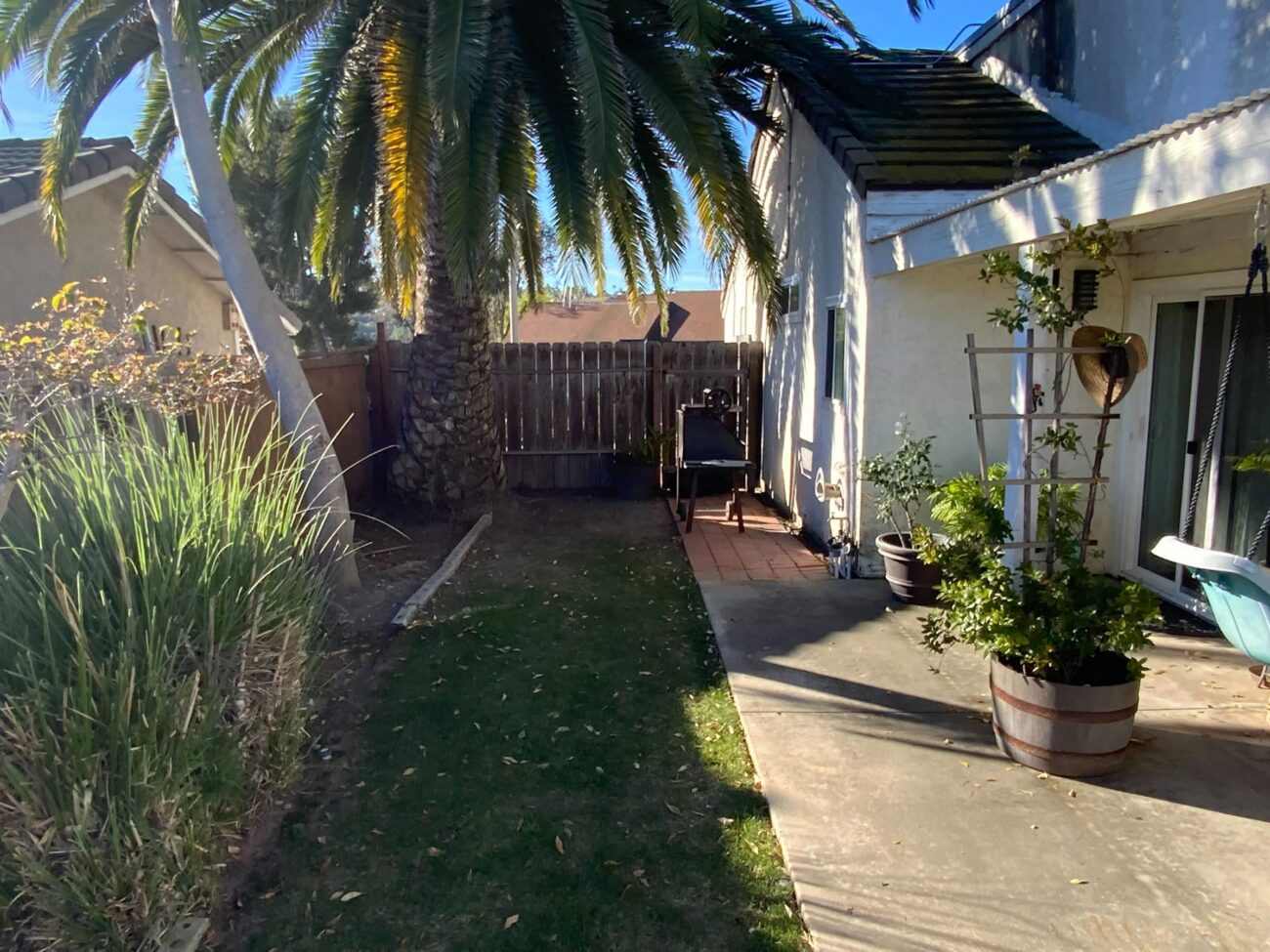 Before: an old freestanding smoker on a brick pad against the house, beside a worn lawn and concrete path.