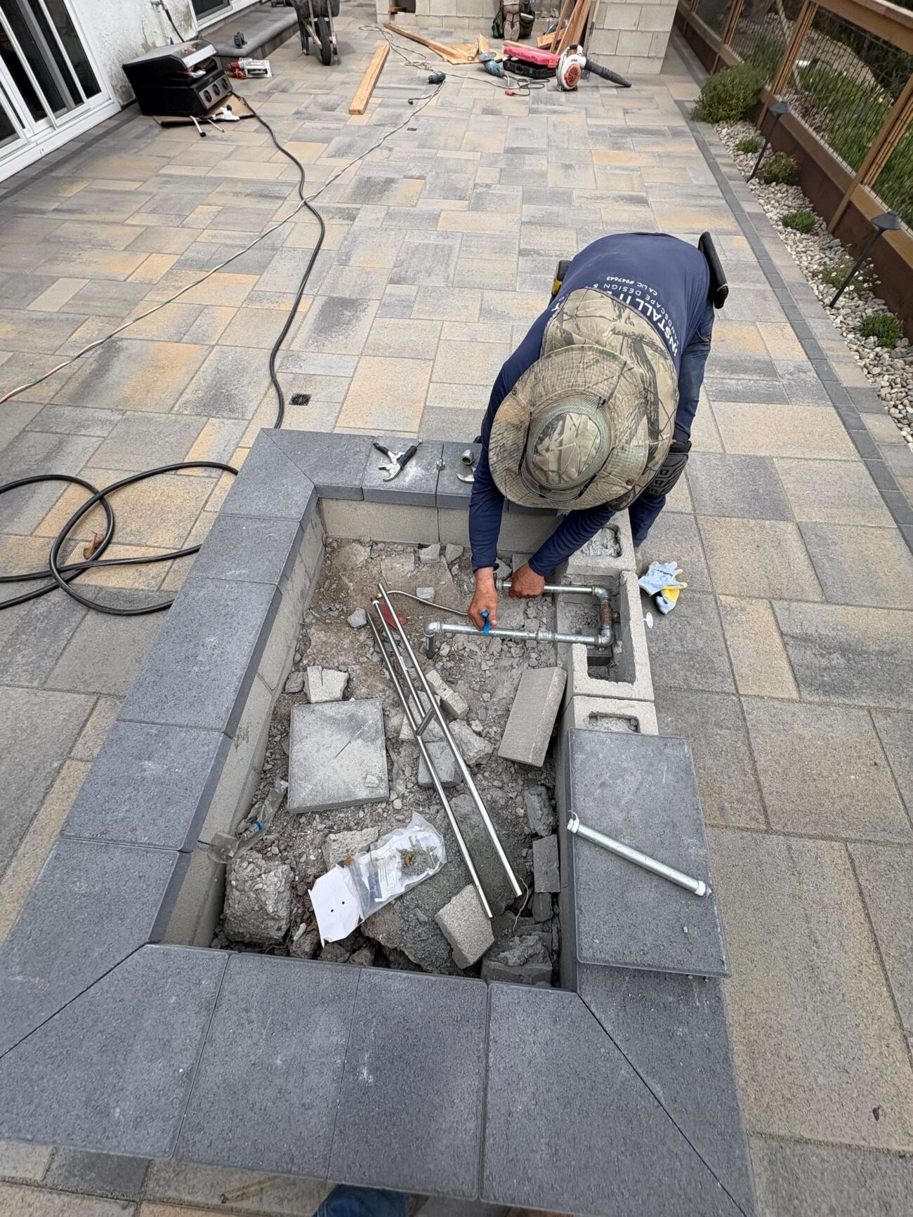 Gas-line and fire-pit components are fitted before the cap stones close the opening.