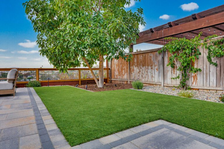 Low-maintenance artificial turf lawn bordered by paver edging and river rock