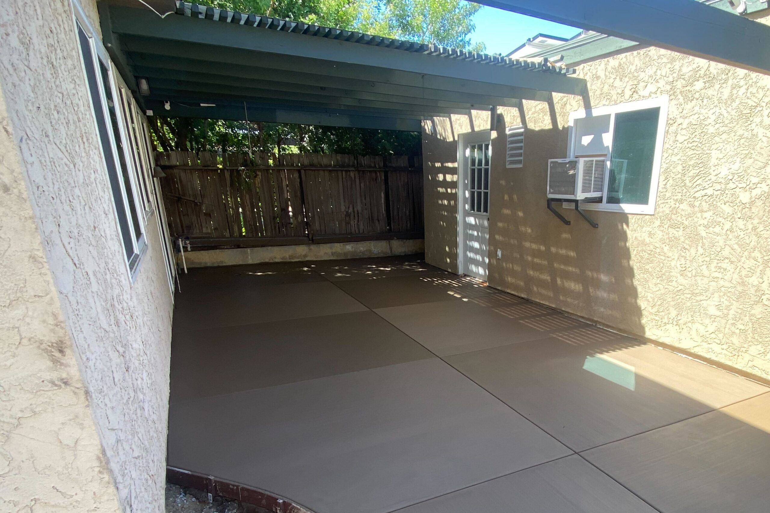 Cropped view of colored concrete patio with saw-cut control joints under the existing pergola in Tierrasanta.