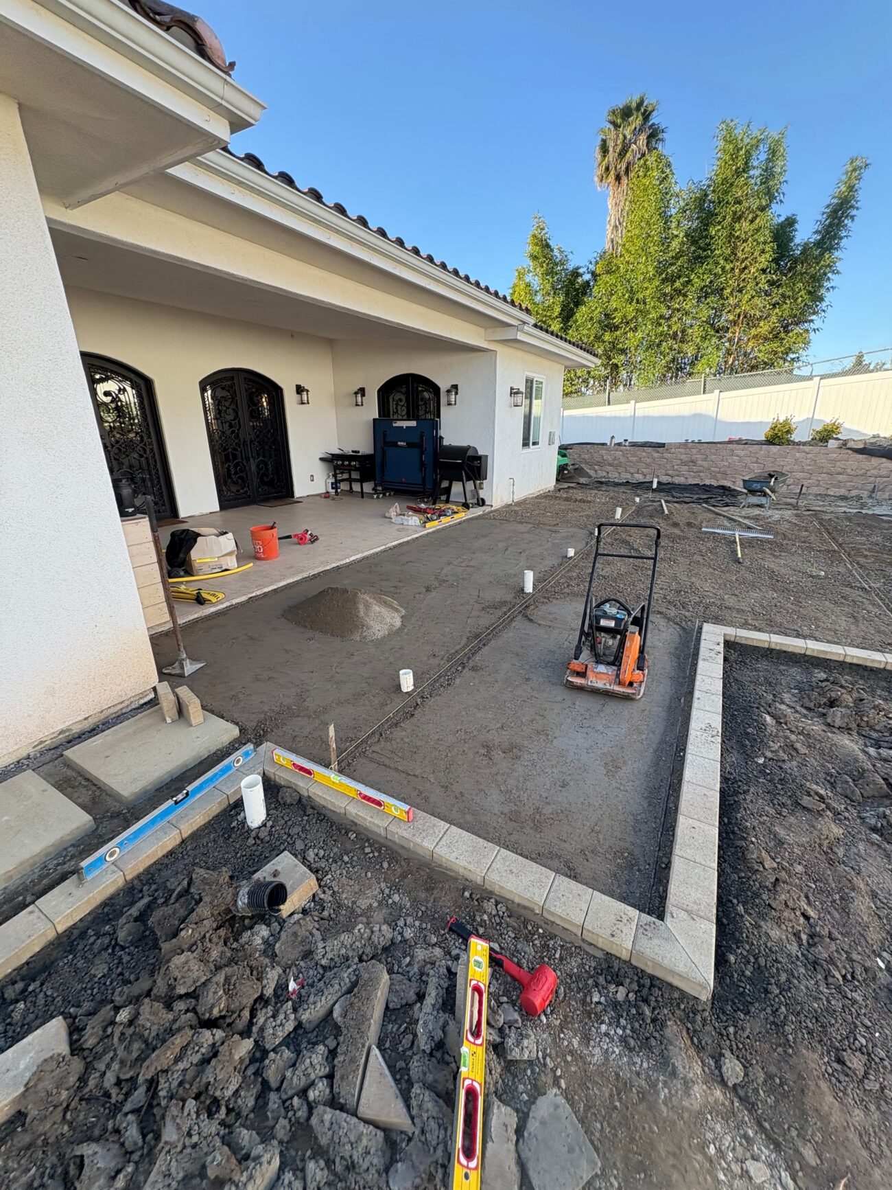 Base preparation for the Vista paver patio: compacted aggregate base, screed rails, and a plate compactor.