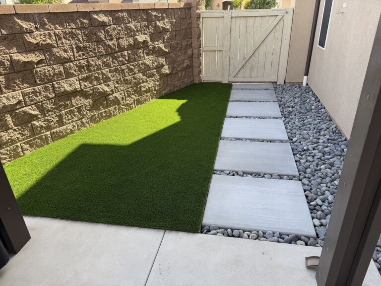 Side yard with a turf strip along a block wall and concrete step pads in black beach pebble beside the house, Escondido 92029