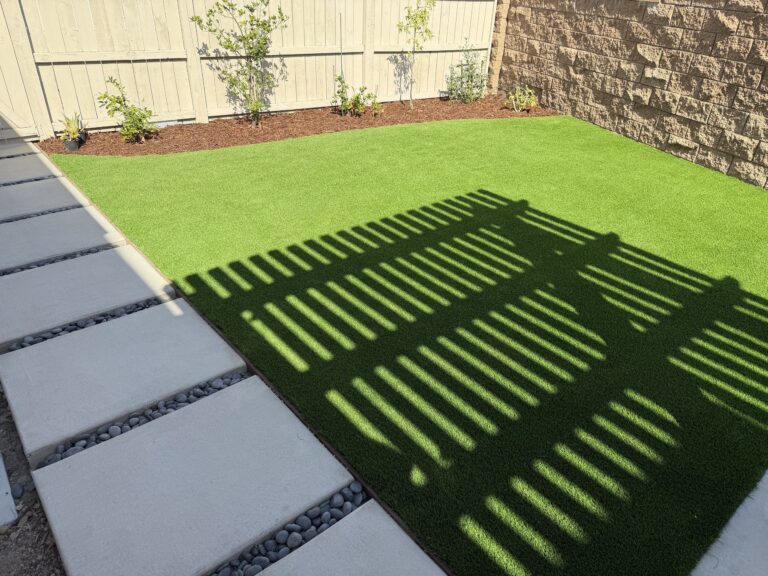 Synthetic turf lawn and a new planting bed along a wood fence, with concrete step pads in beach pebble, Escondido 92029