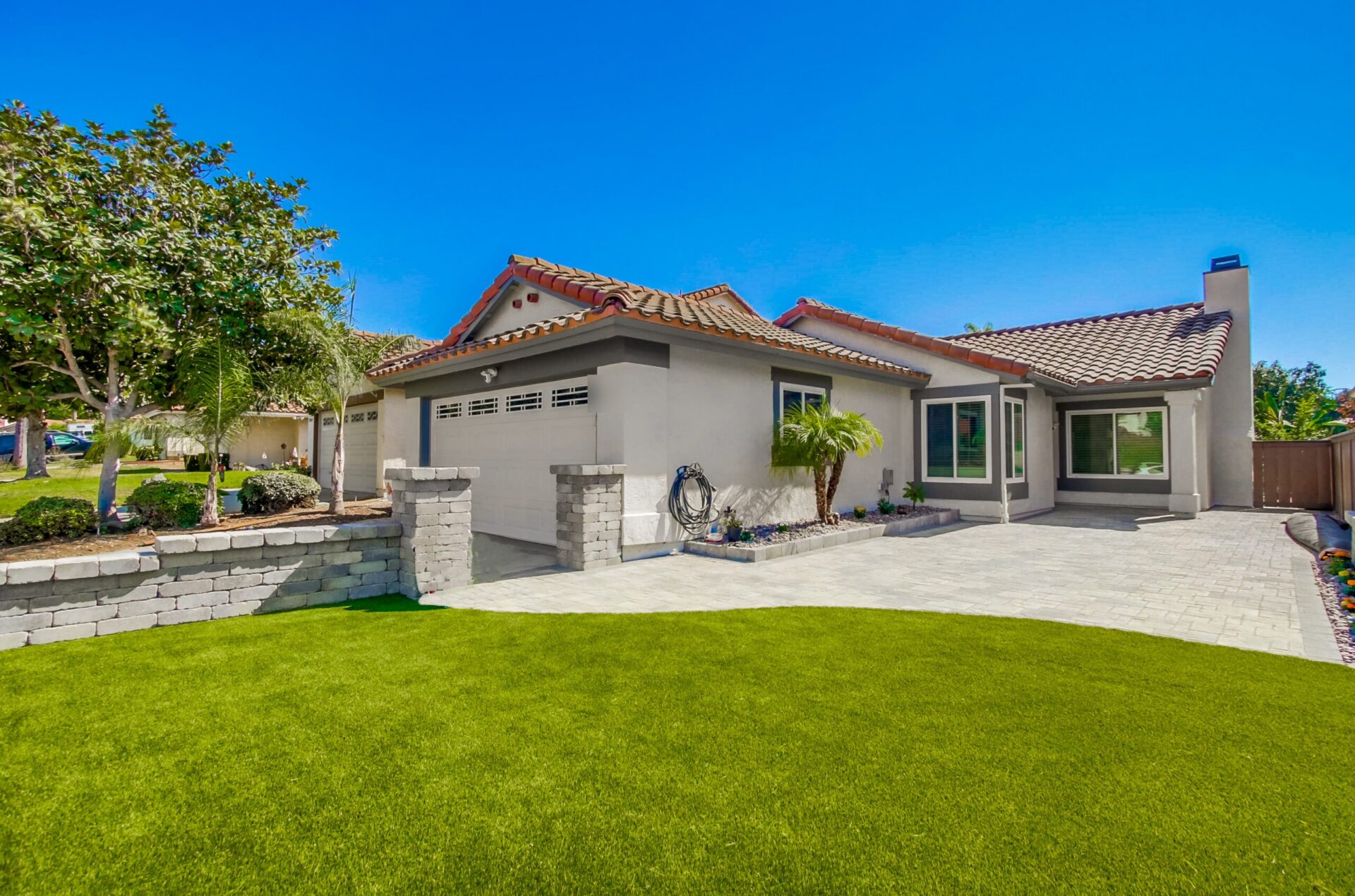Finished Sabre Springs front yard with an Angelus paver driveway, a tiered segmental wall with capped pilasters, and an artificial-turf lawn.