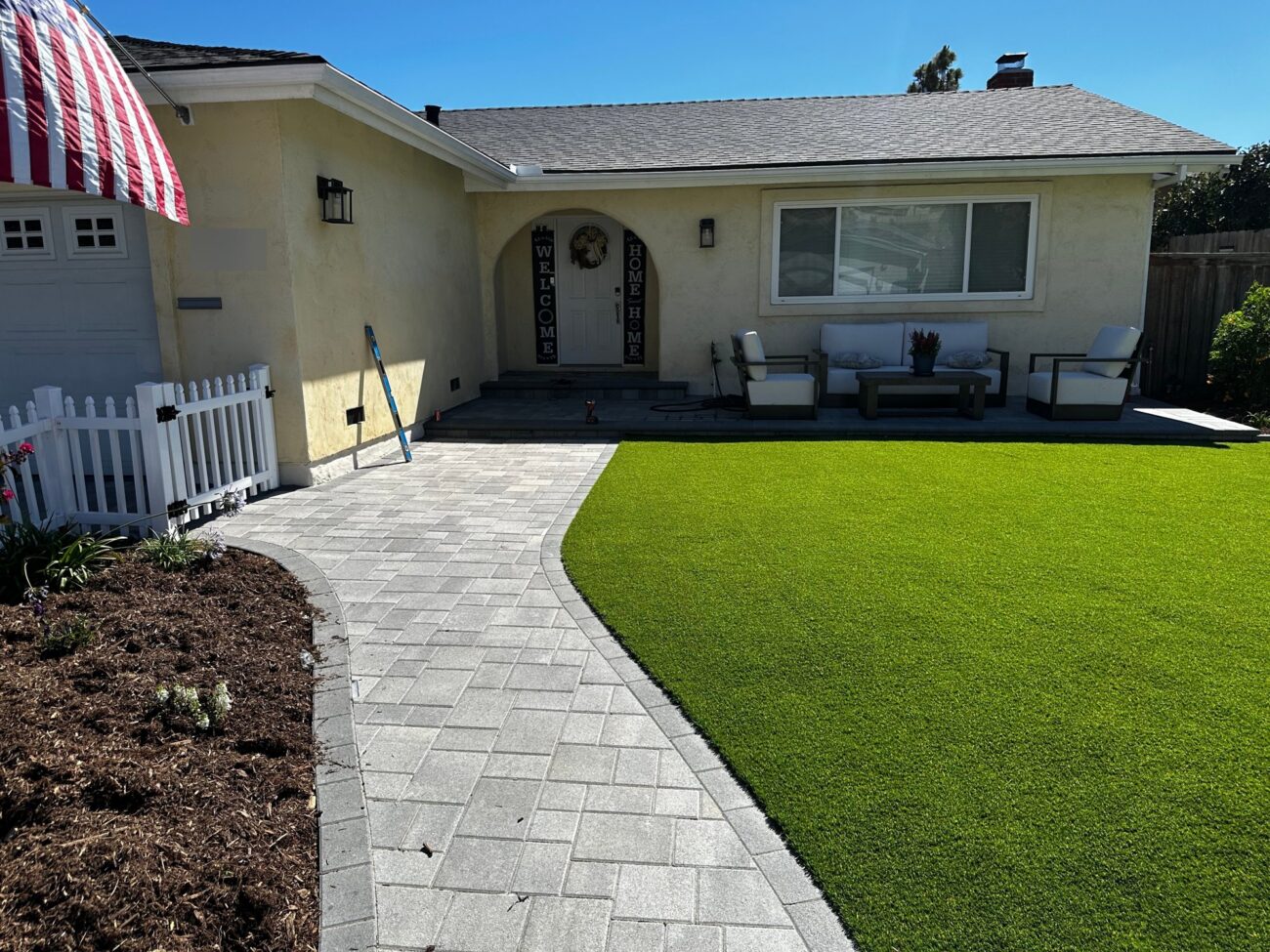 Angelus pavers lead to the front door past new turf and a white picket fence
