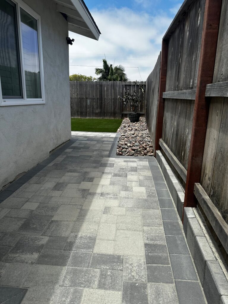 The side yard paving meets the back yard and a river rock bed