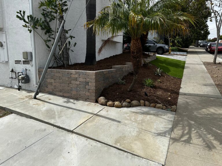 A block retaining wall with new planting and river rock at the side of the house
