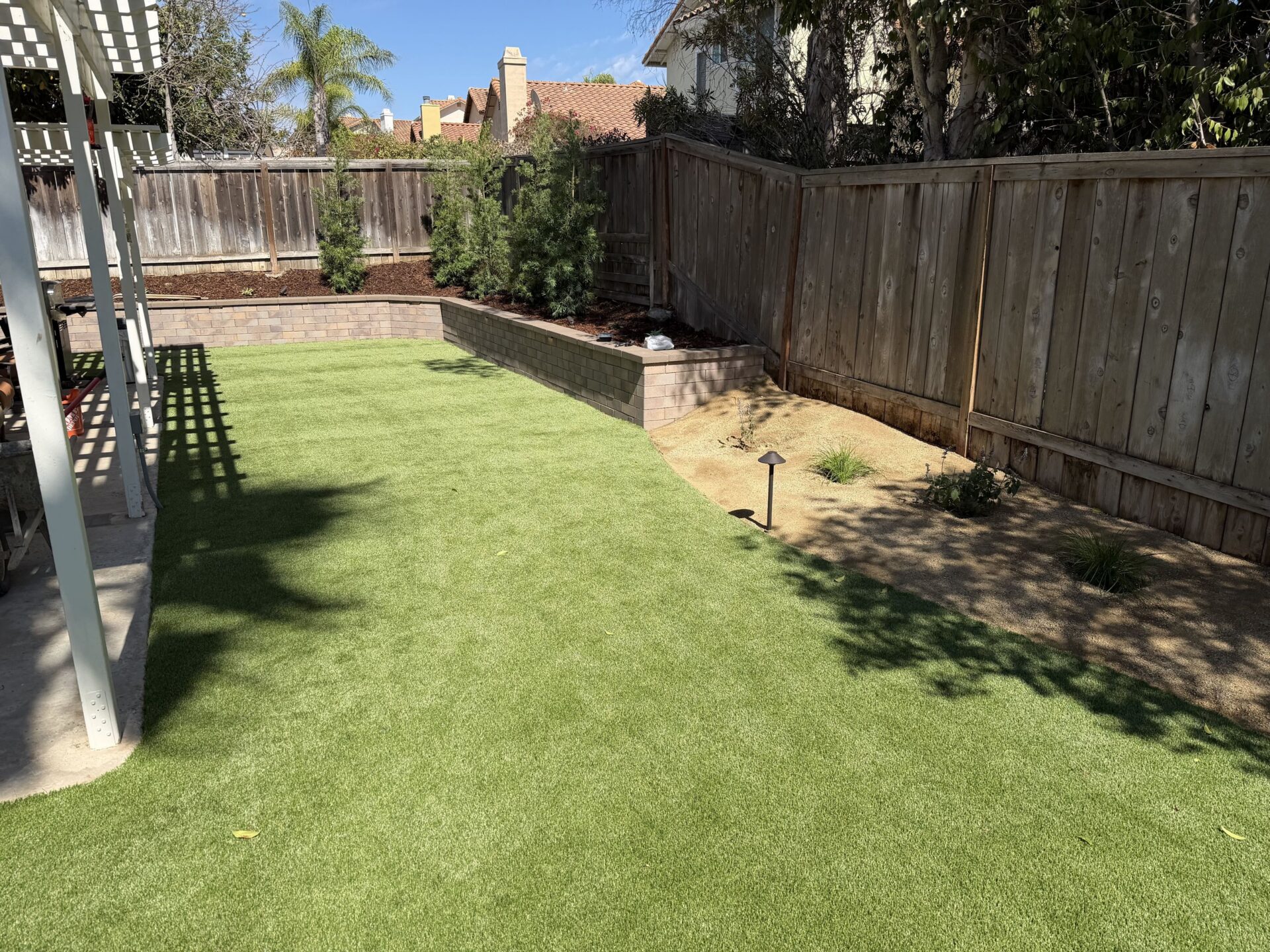 Finished backyard in San Diego 92129: artificial turf framed by a curved Bastione seat and retaining wall with caps, new planting above and decomposed granite beside it