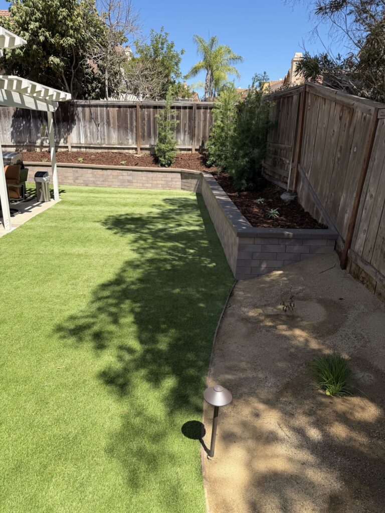 Capped Bastione seat wall turning the corner of the yard, with planting above, turf below and a decomposed granite path