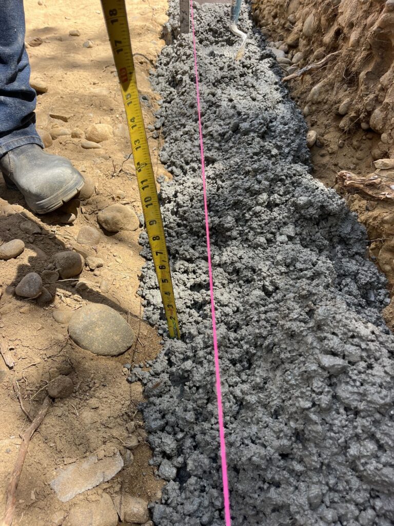 Build stage: the concrete footing for the Bastione wall poured to a string line and checked with a tape